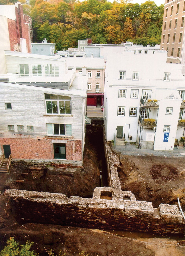 An aerial photo of white building with an archaeological site directly in front of them.