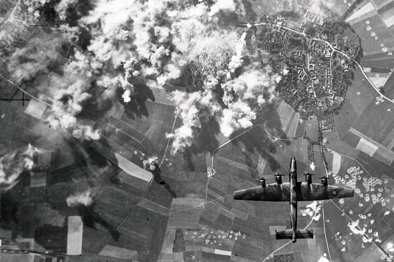 Plumes of smoke rise over a German city as a Halifax bomber completes its bombing run. 