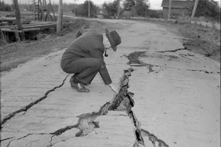 Man in a suit crouching to touch a split in the road