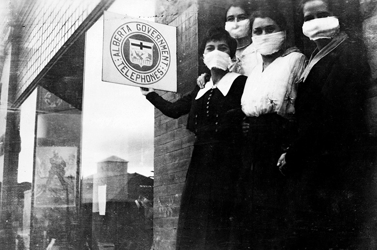 Black and white photo of four women standing on a doorstep wearing masks.