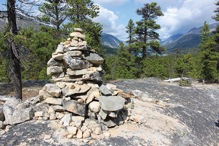 An assemblage of rocks is placed to form a small tower. There are trees in the background.