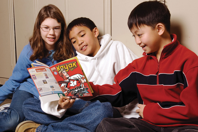 Kids sitting against school lockers pointing out something in Kayak magazine.