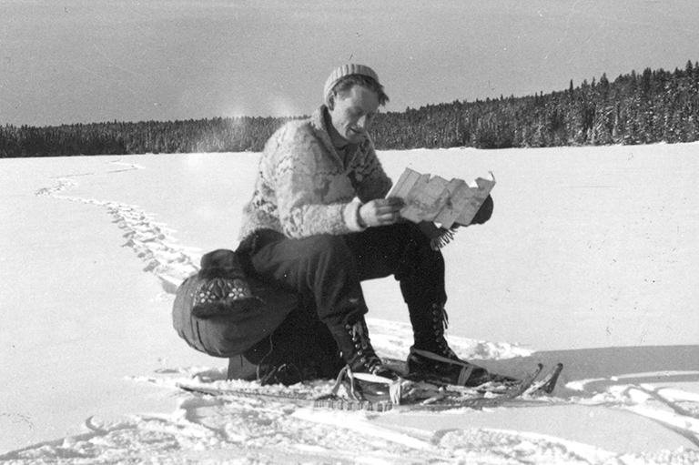 The author pauses to read a map while snowshoeing a northern trapline in 1950.