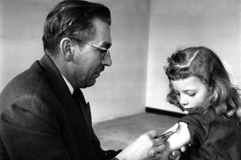 Black and white photo of a man administering a vaccine to a young girl.